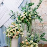 Elegant wedding decor at 128 South, featuring a stylish draped backdrop in blue and white, set against the venue's brick wall with beautiful floral arrangements.
