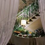 Wedding decor on the historic staircase at 128 South, featuring green garlands wrapped around the white railings and soft, romantic lighting.