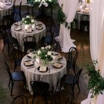 White and green floral centerpieces with candles on wedding reception tables, with soft draping and decor for a Wilmington, NC even